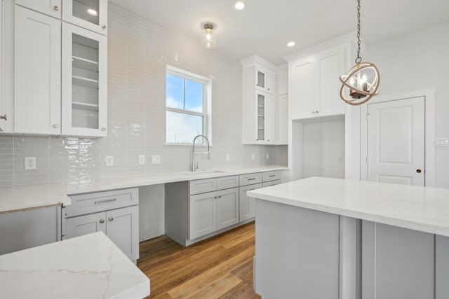 26726 Estuary Dr, Galveston, TX 77554 - kitchen with decorative light fixtures, backsplash, glass insert cabinets, a sink, and light wood-type flooring