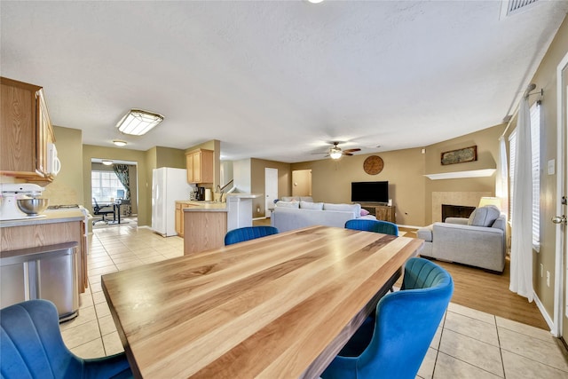 dining space featuring light tile patterned floors, a tiled fireplace, visible vents, and baseboards