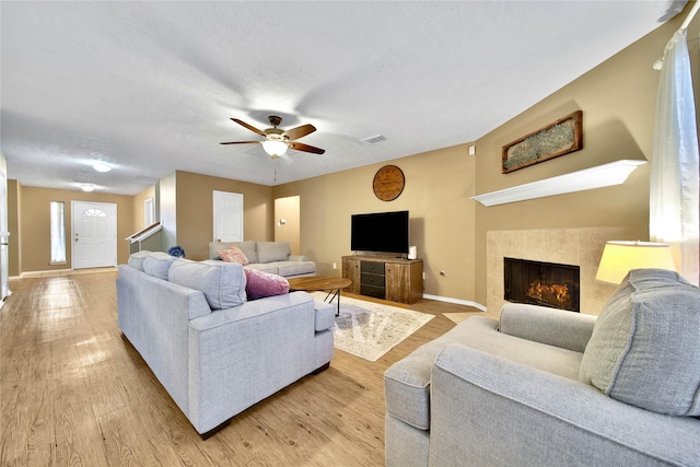 living room featuring baseboards, visible vents, a textured ceiling, light wood-style floors, and a fireplace