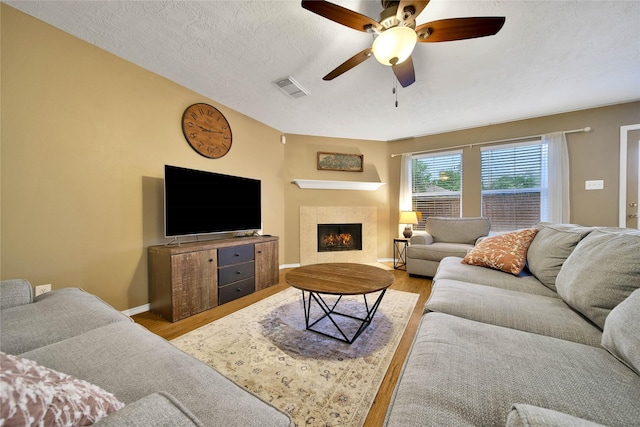 living room featuring a textured ceiling, ceiling fan, wood finished floors, visible vents, and a tiled fireplace