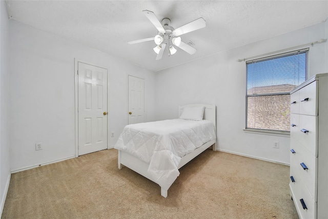 bedroom featuring a ceiling fan, light colored carpet, and a textured ceiling