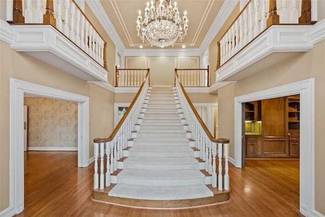 staircase featuring a towering ceiling, crown molding, and wood finished floors