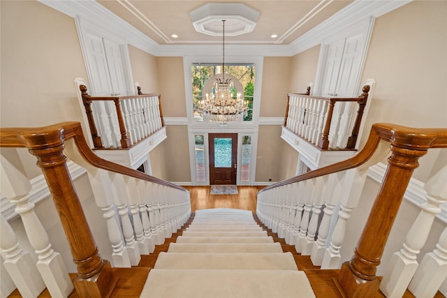 stairway with an inviting chandelier, crown molding, a wealth of natural light, and wood finished floors