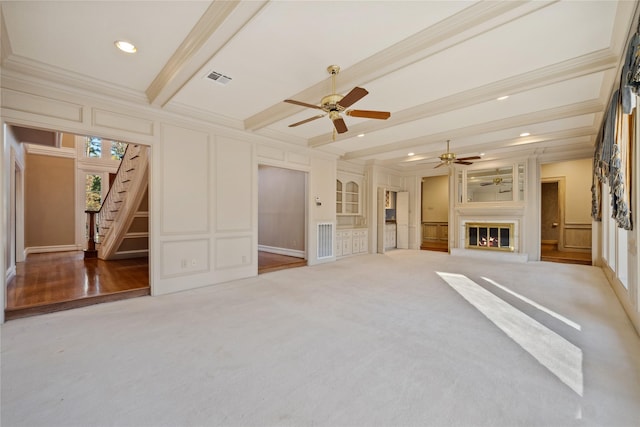 unfurnished living room with beam ceiling, crown molding, a decorative wall, a glass covered fireplace, and stairs