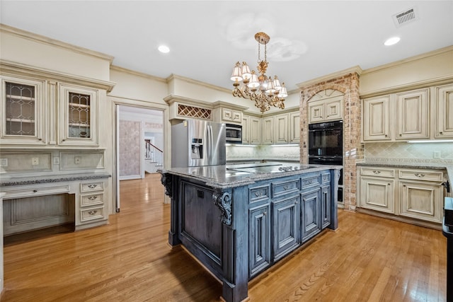 kitchen featuring black appliances, cream cabinets, light wood-style flooring, and an inviting chandelier