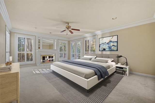 bedroom featuring carpet flooring, a ceiling fan, baseboards, a glass covered fireplace, and crown molding