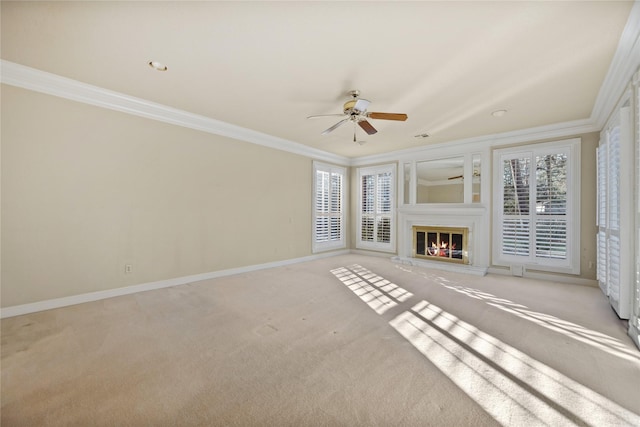 unfurnished living room featuring a glass covered fireplace, carpet flooring, crown molding, and baseboards