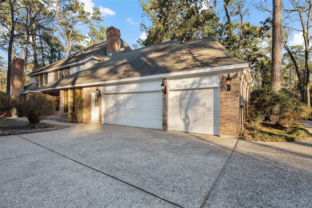 view of property exterior featuring a garage, driveway, a chimney, roof with shingles, and brick siding