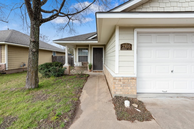 view of exterior entry featuring a garage, roof with shingles, a lawn, and brick siding