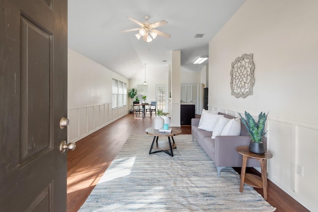 living room featuring lofted ceiling, visible vents, wood finished floors, and wainscoting