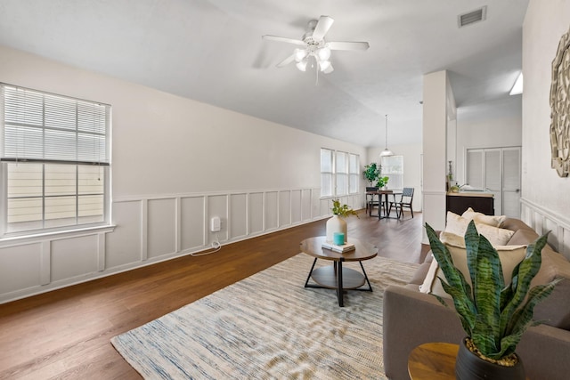 living room with lofted ceiling, a decorative wall, wood finished floors, a ceiling fan, and visible vents