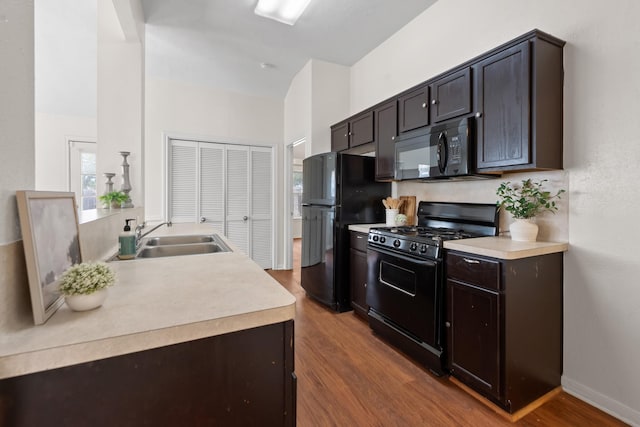 kitchen with a sink, black appliances, light countertops, and wood finished floors