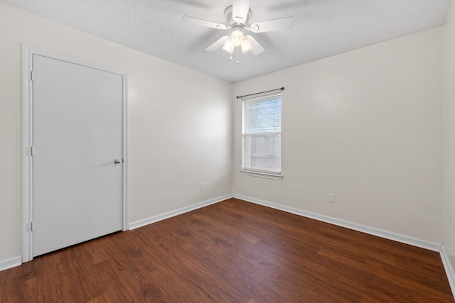 spare room featuring baseboards, a ceiling fan, and dark wood-type flooring