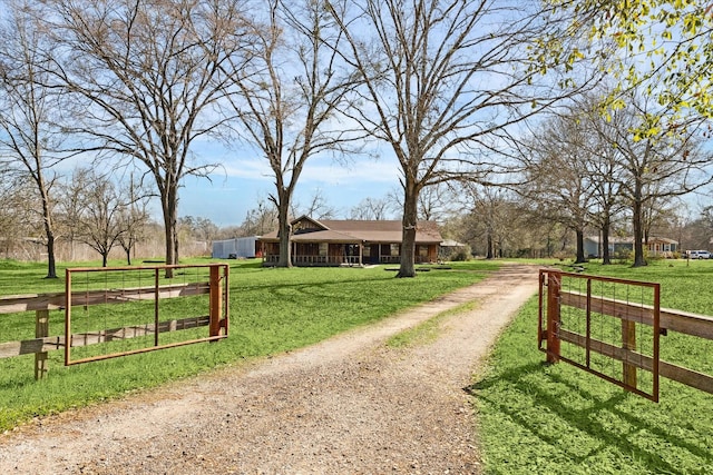 view of community with dirt driveway, a rural view, and a yard