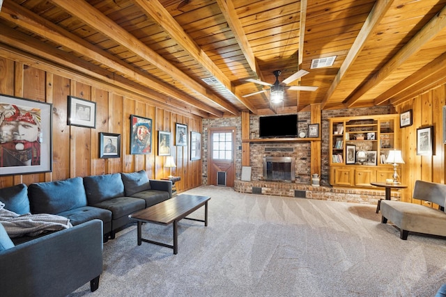 carpeted living area featuring beam ceiling, visible vents, a brick fireplace, wooden walls, and wooden ceiling