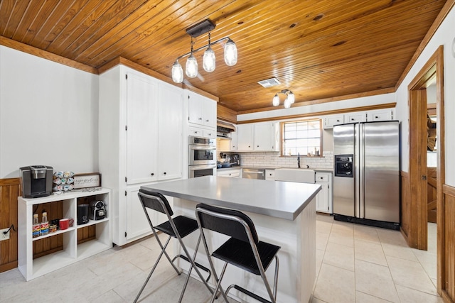 kitchen featuring appliances with stainless steel finishes, white cabinets, decorative light fixtures, and a kitchen island