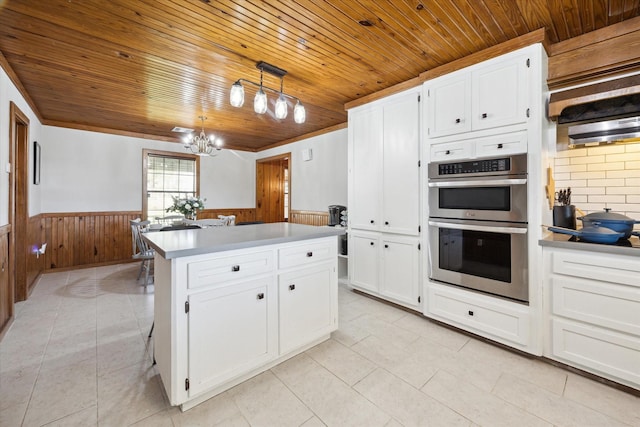 kitchen featuring stainless steel double oven, a wainscoted wall, white cabinetry, a center island, and pendant lighting