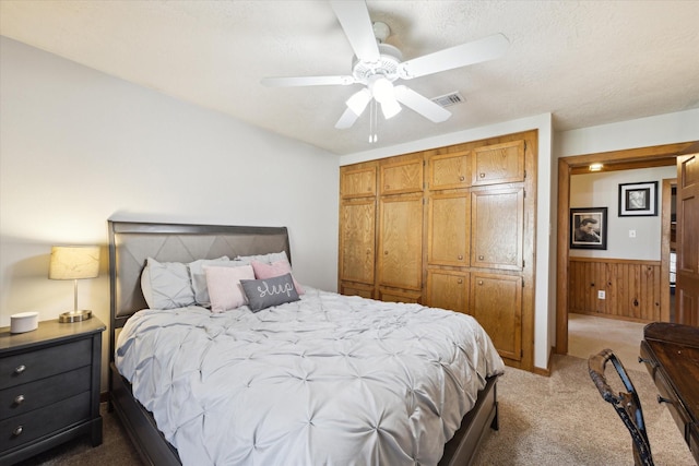 carpeted bedroom featuring ceiling fan, a textured ceiling, a wainscoted wall, wood walls, and visible vents