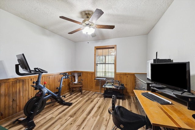 interior space with a textured ceiling, light wood-type flooring, wainscoting, and a ceiling fan