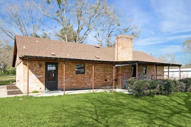 rear view of house with a shingled roof, brick siding, a yard, and a chimney