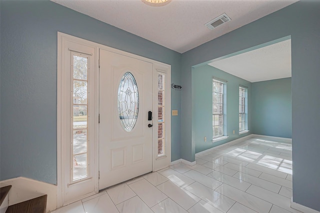 foyer entrance with a wealth of natural light, visible vents, baseboards, and light tile patterned floors