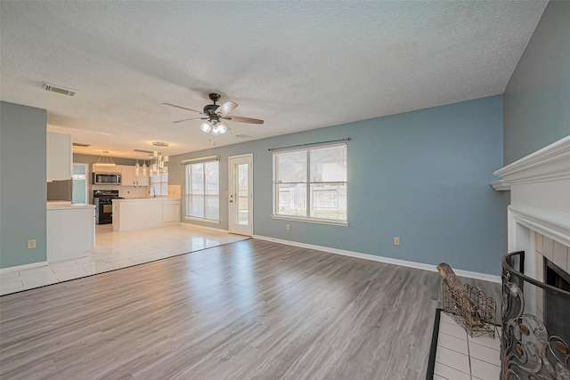 unfurnished living room featuring light wood-type flooring, a textured ceiling, a ceiling fan, and a tiled fireplace