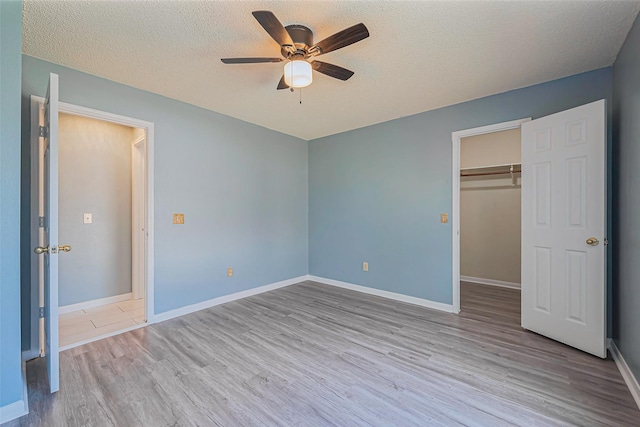 unfurnished bedroom featuring a walk in closet, wood finished floors, baseboards, and a textured ceiling