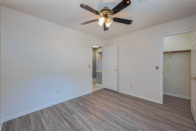 unfurnished bedroom featuring a ceiling fan, a textured ceiling, wood finished floors, a closet, and baseboards