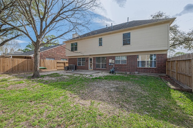 rear view of house with brick siding, a fenced backyard, a lawn, and a patio area