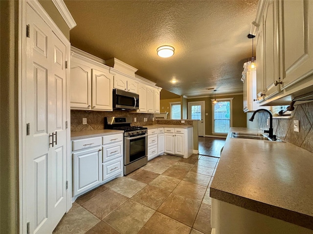 kitchen featuring a peninsula, stainless steel appliances, white cabinetry, pendant lighting, and a sink