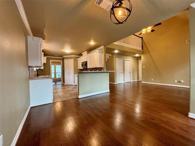 kitchen with stainless steel microwave, ornamental molding, open floor plan, white cabinets, and a sink