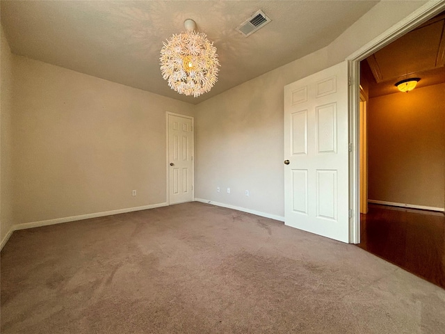 spare room featuring dark colored carpet, visible vents, a notable chandelier, and baseboards