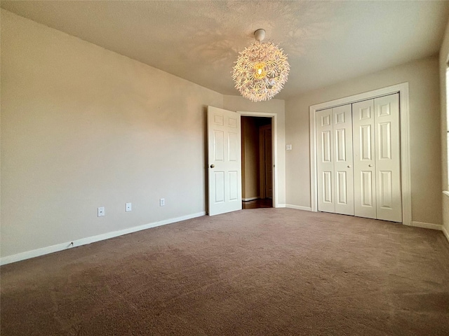 unfurnished bedroom featuring a chandelier, a closet, carpet flooring, and baseboards