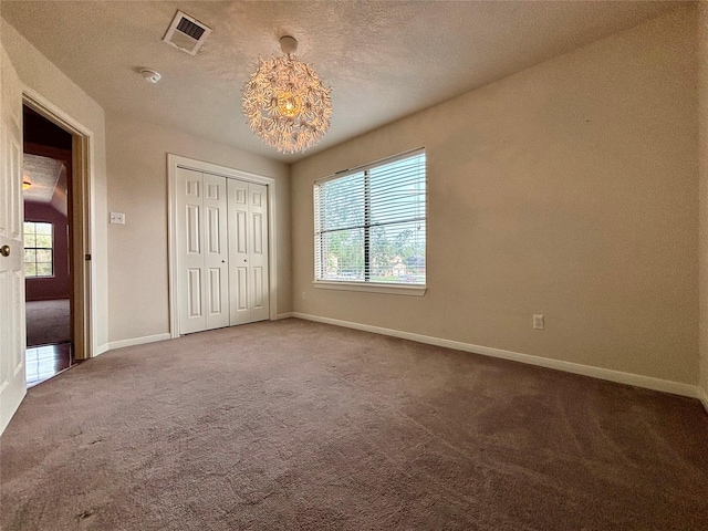 unfurnished bedroom featuring a textured ceiling, carpet flooring, visible vents, baseboards, and a closet