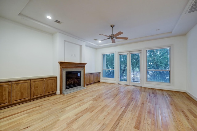 unfurnished living room featuring visible vents, a tray ceiling, and a glass covered fireplace