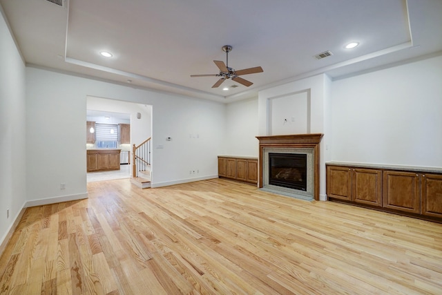 unfurnished living room featuring stairway, light wood-type flooring, a raised ceiling, and visible vents