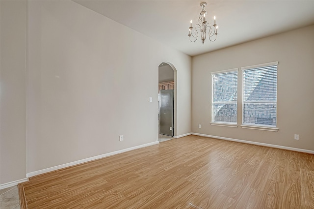 spare room with a notable chandelier, light wood-style flooring, and baseboards