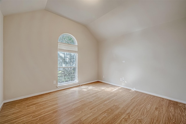 empty room with light wood-style floors, lofted ceiling, and baseboards