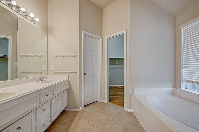 bathroom featuring double vanity, a garden tub, tile patterned flooring, a walk in closet, and a sink