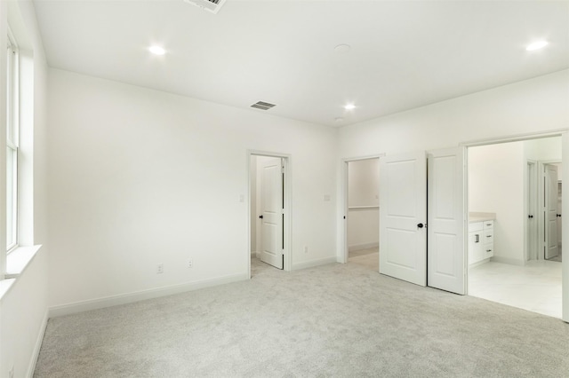 unfurnished bedroom featuring a spacious closet, recessed lighting, light colored carpet, and visible vents