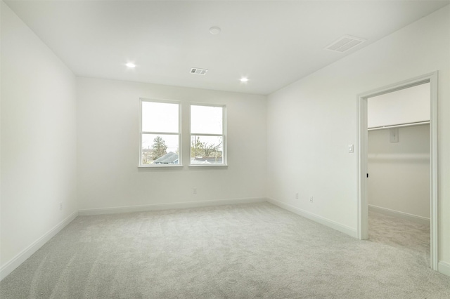 unfurnished bedroom with light carpet, visible vents, recessed lighting, and a walk in closet