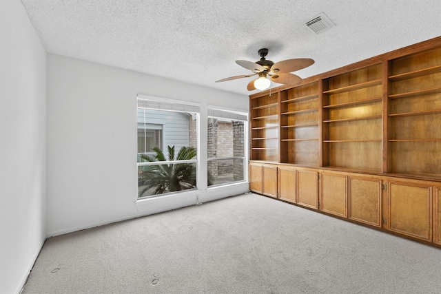 empty room with light carpet, ceiling fan, a textured ceiling, and visible vents