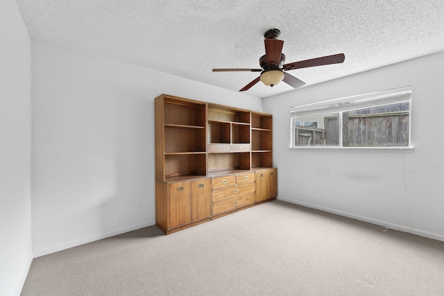 unfurnished room featuring light carpet, ceiling fan, a textured ceiling, and baseboards