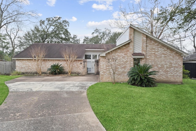 mid-century inspired home with driveway, brick siding, a front yard, and fence