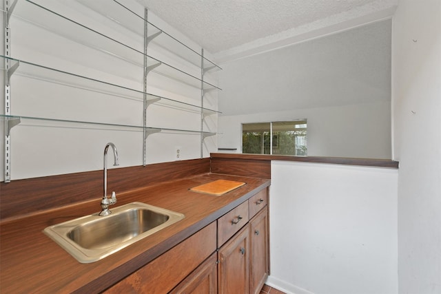 kitchen with dark countertops, a textured ceiling, brown cabinetry, and a sink