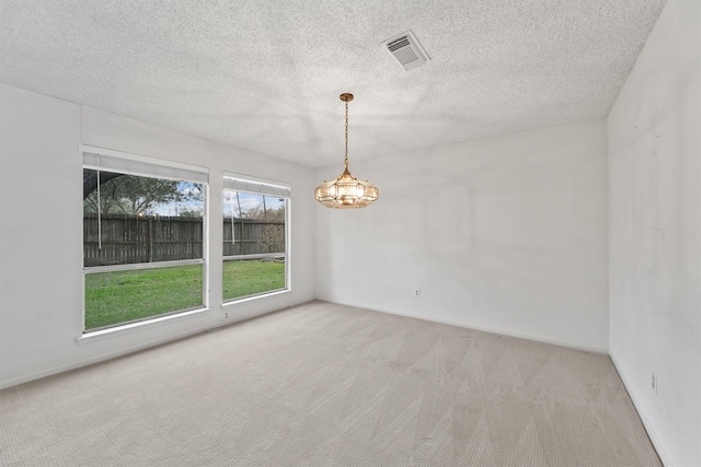 spare room with visible vents, an inviting chandelier, light carpet, a textured ceiling, and baseboards