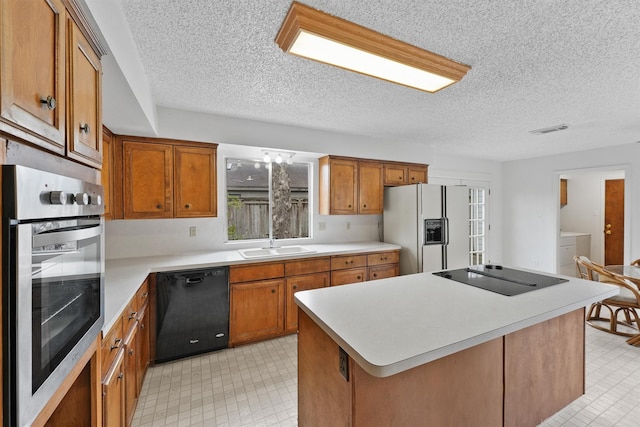 kitchen with brown cabinetry, light countertops, a kitchen island, and black appliances