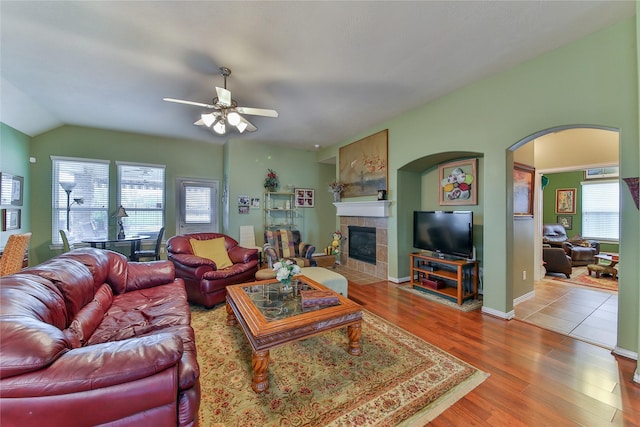 living area with arched walkways, a tile fireplace, wood finished floors, a ceiling fan, and vaulted ceiling