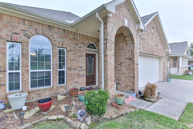 property entrance featuring a garage, concrete driveway, brick siding, and roof with shingles