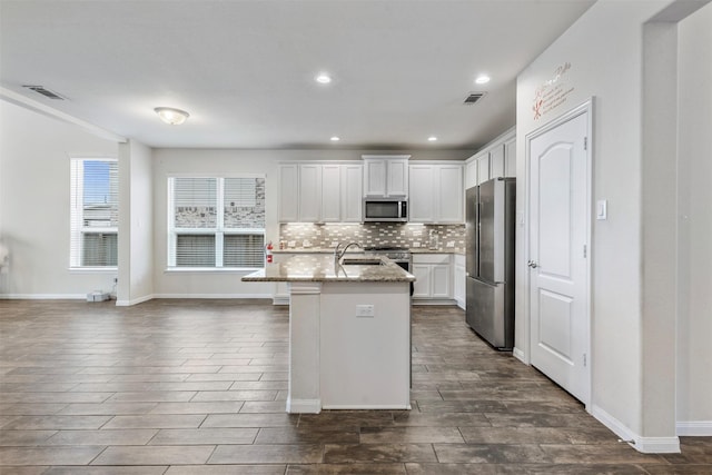 kitchen with visible vents, white cabinets, light stone countertops, a kitchen island with sink, and stainless steel appliances